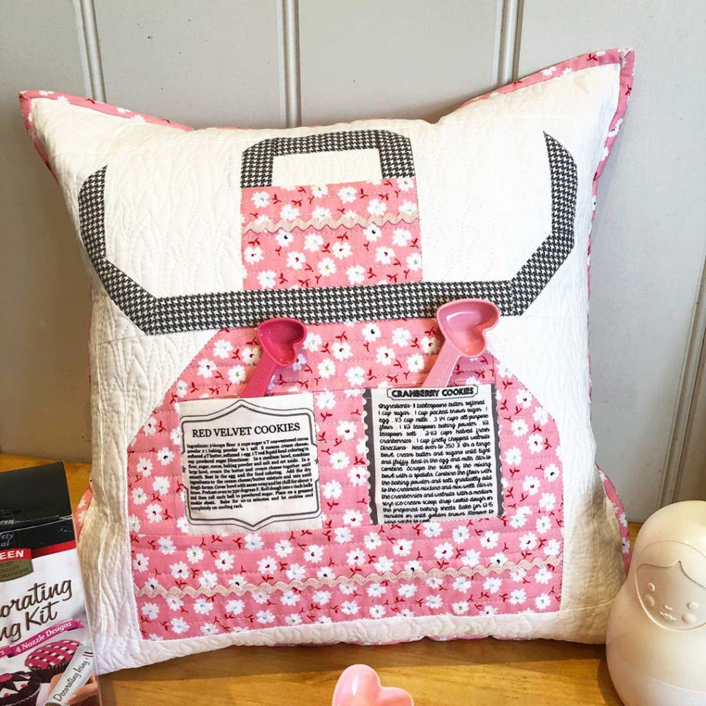 Anne sewed a quilt block inot a pillow. The block features an apron with recipes on the pockets.