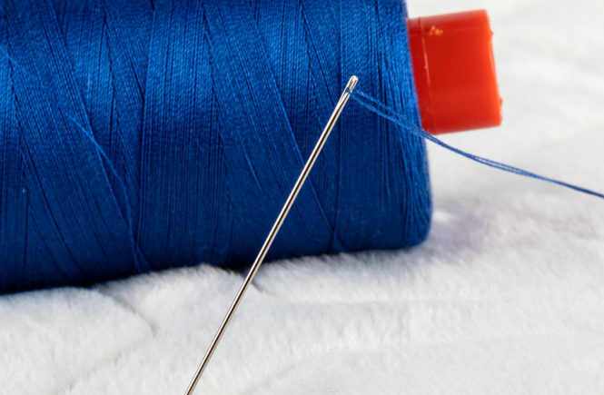 Sewing needle threaded with blue thread