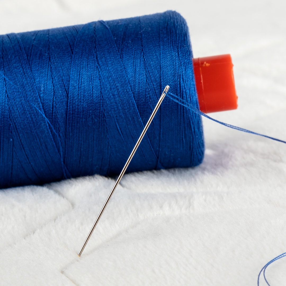 Hand sewing needle threaded with blue thread