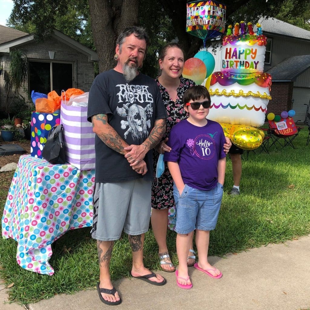 Eilidh and her parents are smiling standing on their front yard, celebrating Eilidh's birthday! 