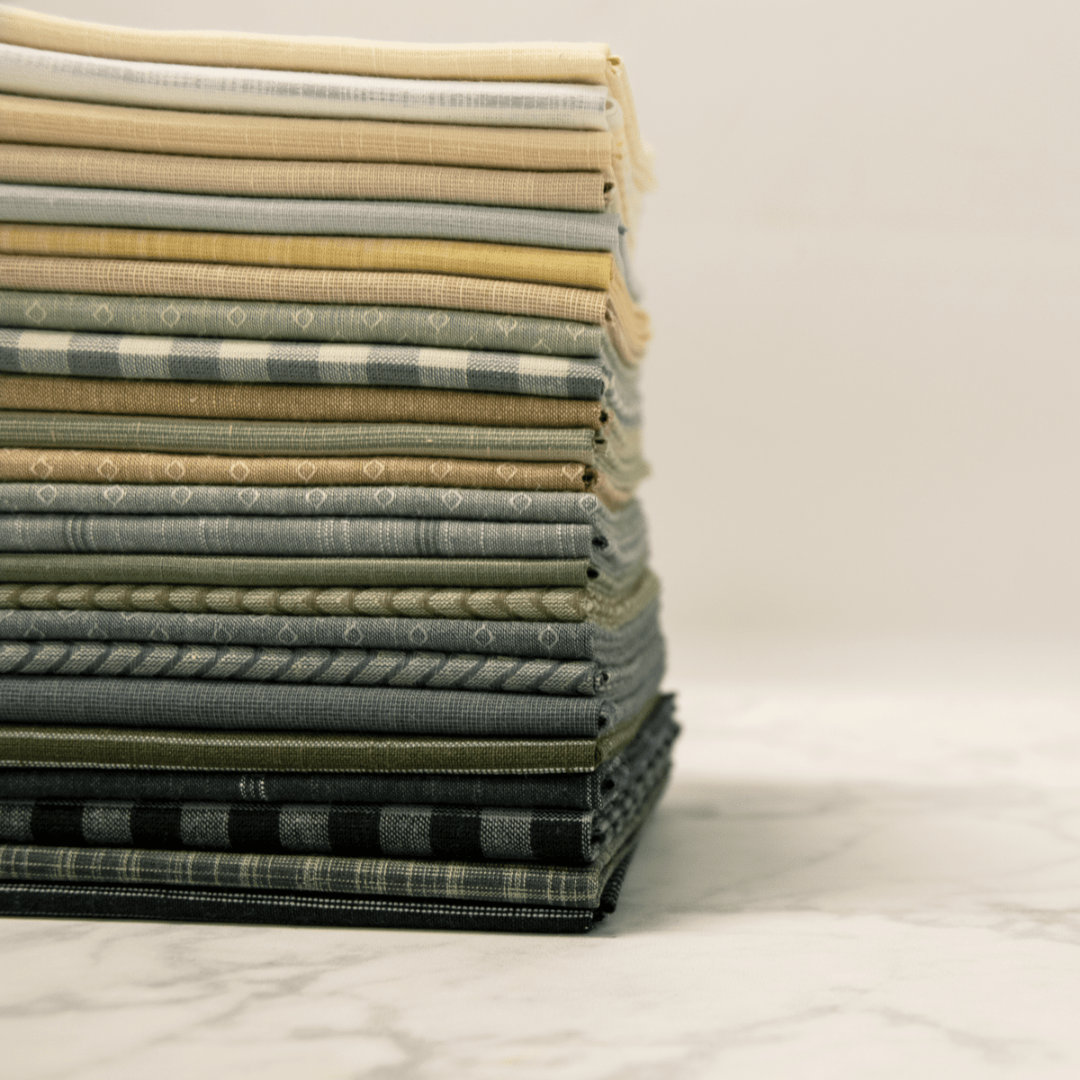 A Stack of Compass woven fabrics by Laundry Basket Quilts showing the texture and weave of this quilting fabric type