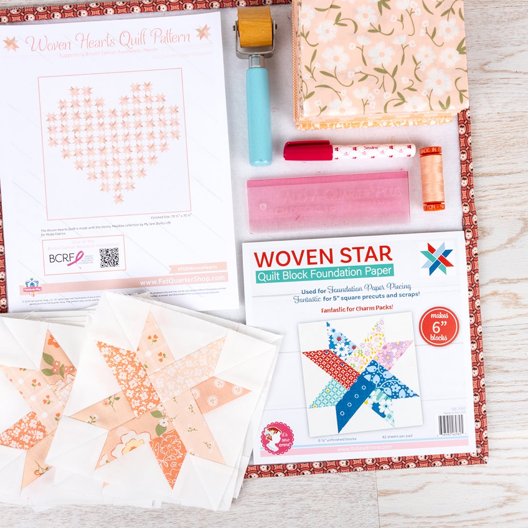 A flat lay with the woven star foundation paper pack, the quilt pattern, finished woven star blocks, a sewline glue pen, peach thread, a seam roller, and an add-a-quarter ruler set on a design board