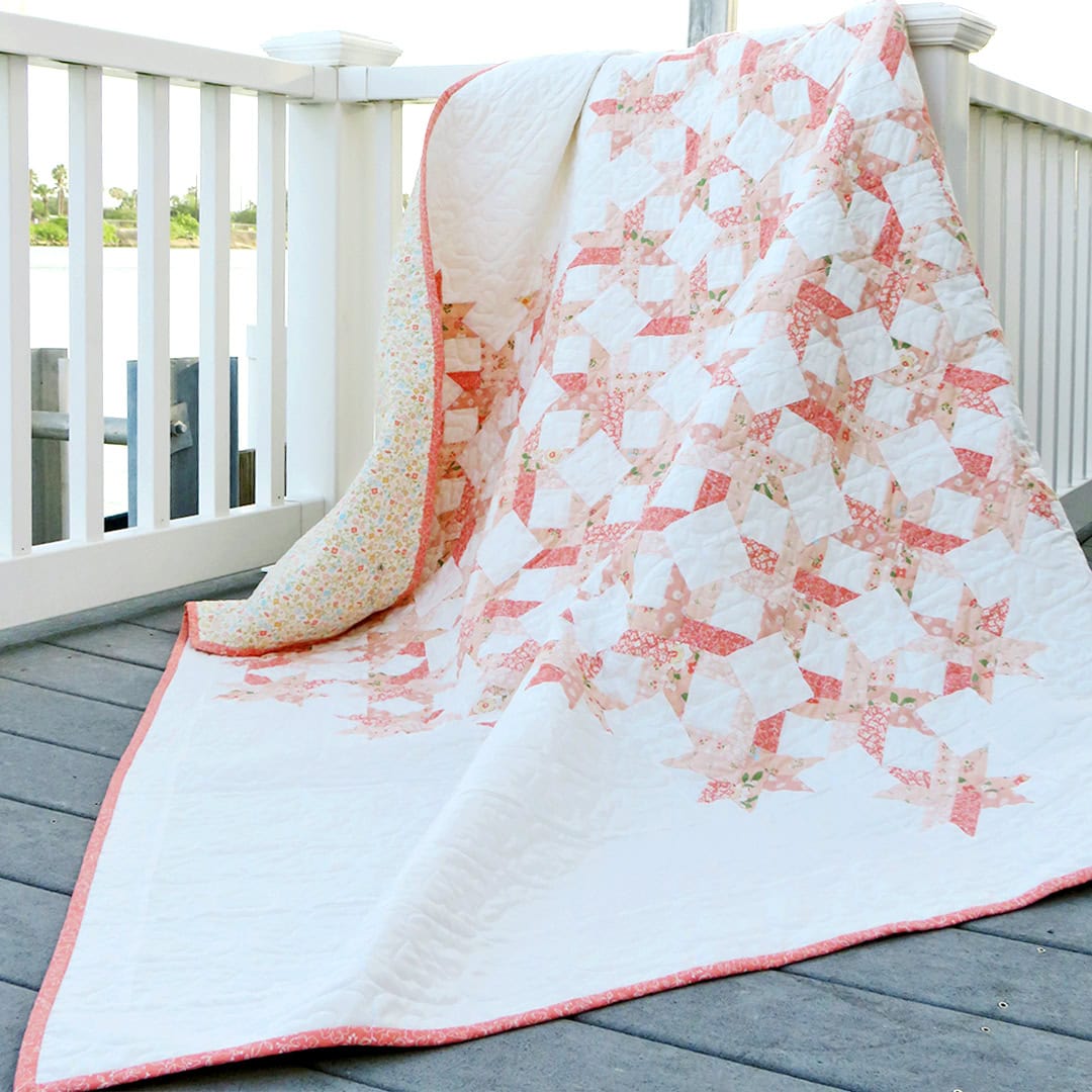 Gina Tell's finished Woven Hearts Quilt pictured draped over white railing on a porch overlooking water